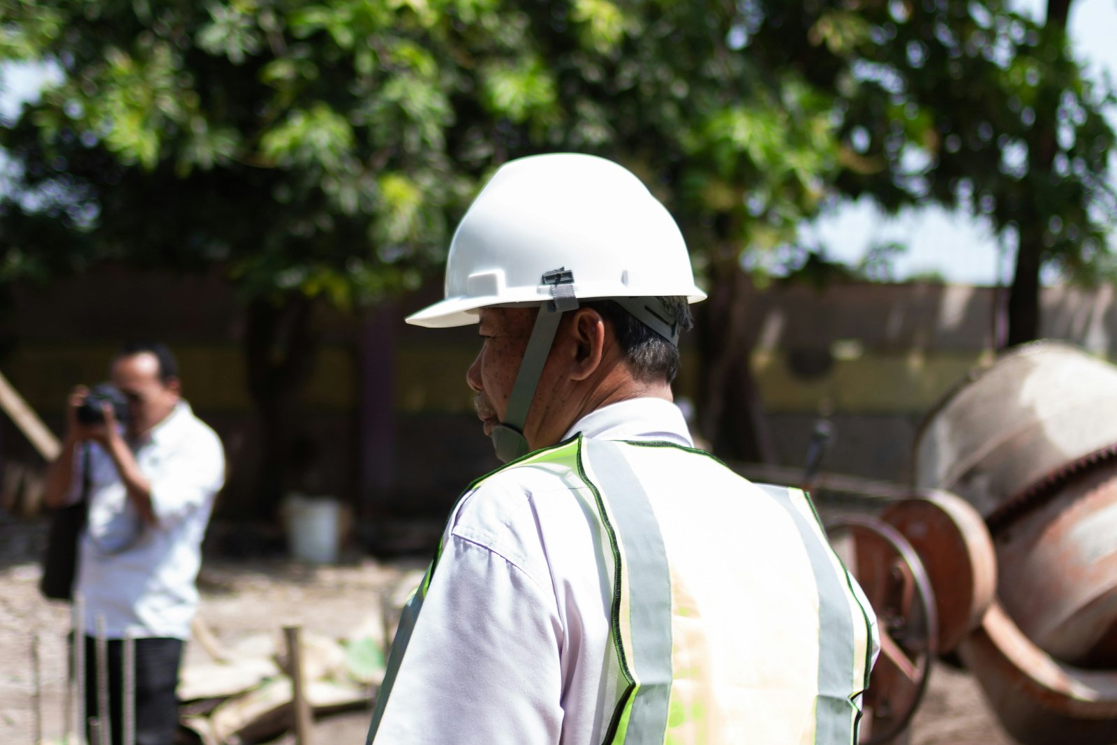 Coordinateur Kọilé en gilet et casque sur un chantier en cours, plans à la main, latérite rouge visible au sol