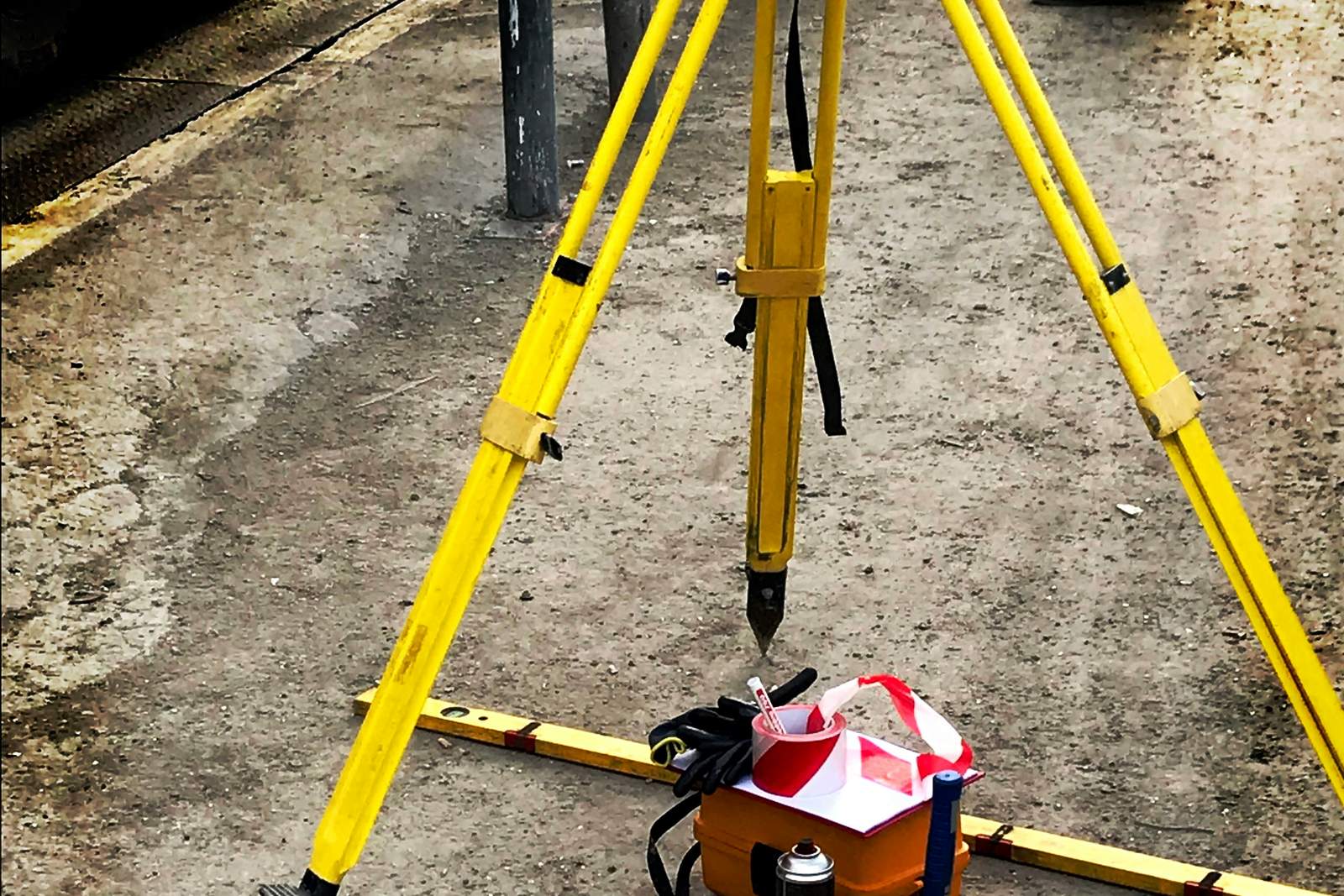 Géomètre en gilet jaune avec trépied et tachéomètre planté dans une parcelle en latérite