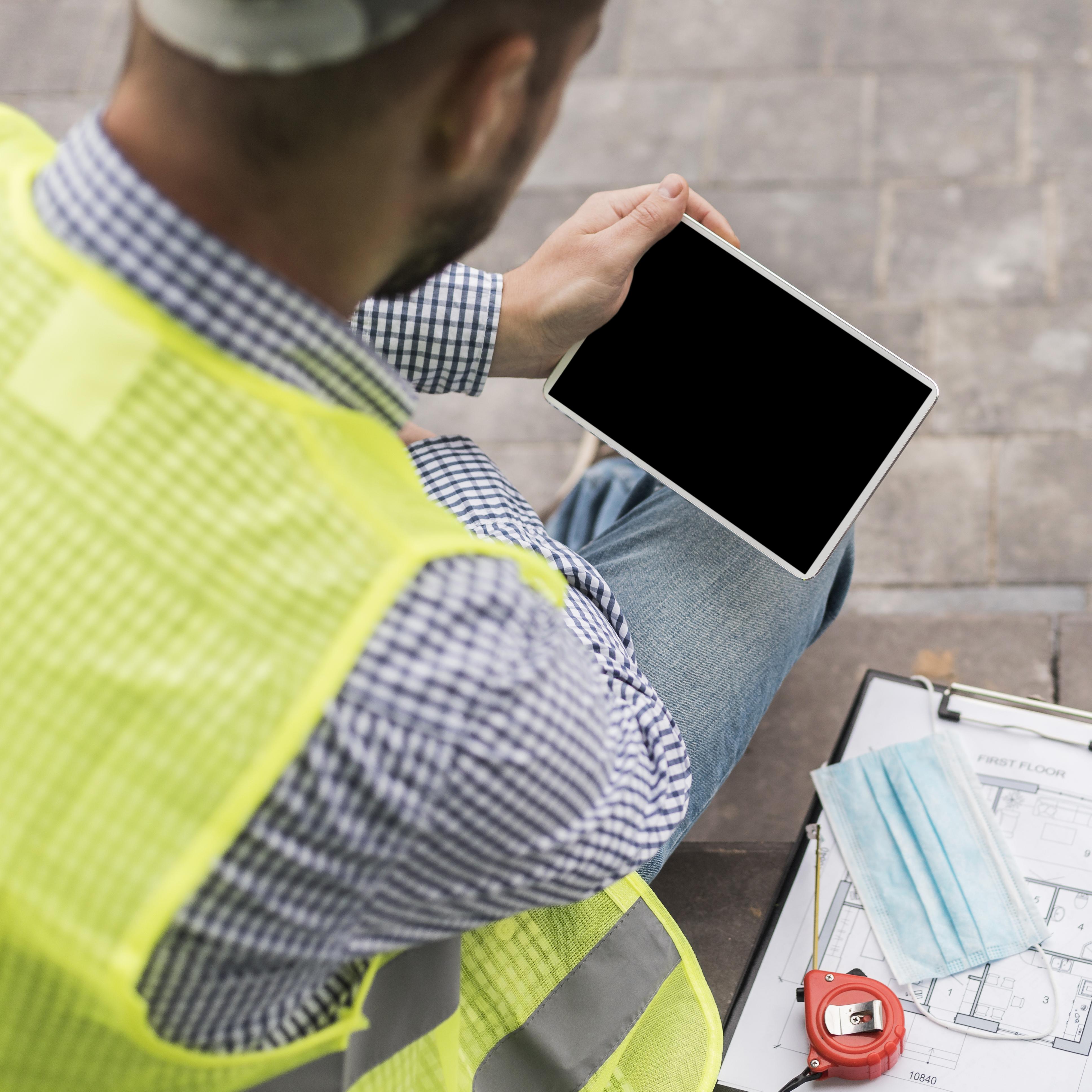 Mains annotant un plan d’architecte à côté d’un casque de chantier et d’un téléphone affichant une carte
